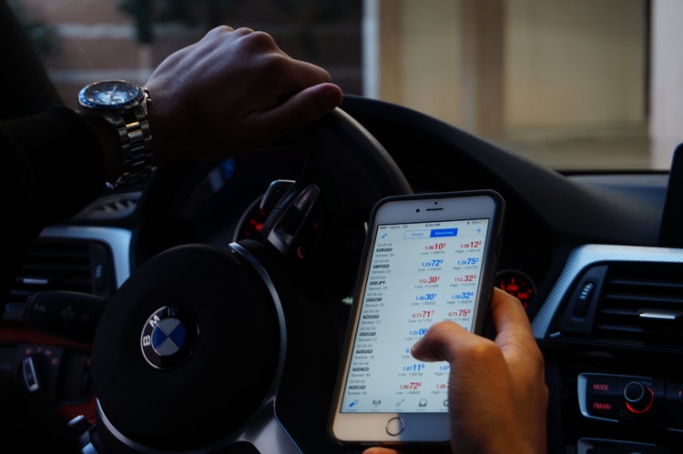 person in car looking at forex app on mobile phone